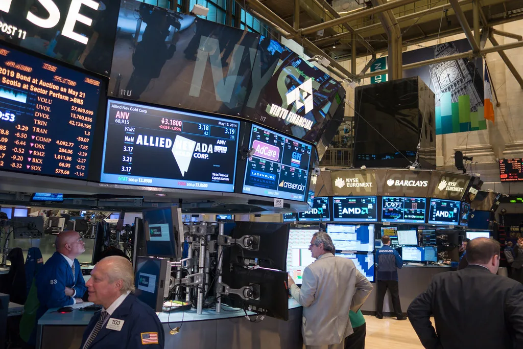 Traders on a stock exchange floor beneath electronic display boards showing index levels